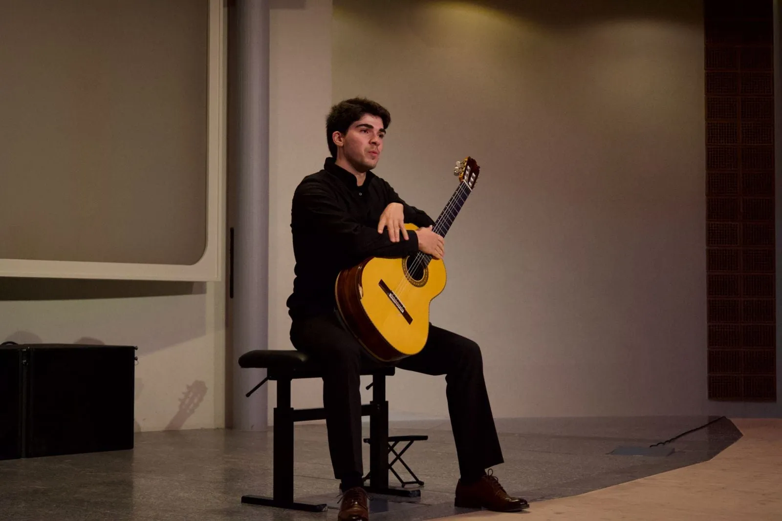 Miguel Ferreira seated and playing, in a black shirt, on a bare stage.