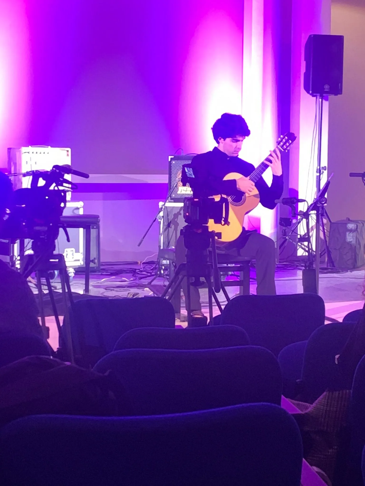 Miguel Ferreira on stage under violet light at Guitar Days, film cameras in the foreground.