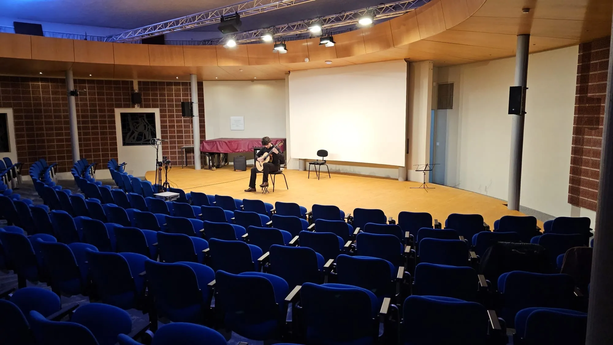 A concert hall with blue seats, Miguel Ferreira playing in the distance.