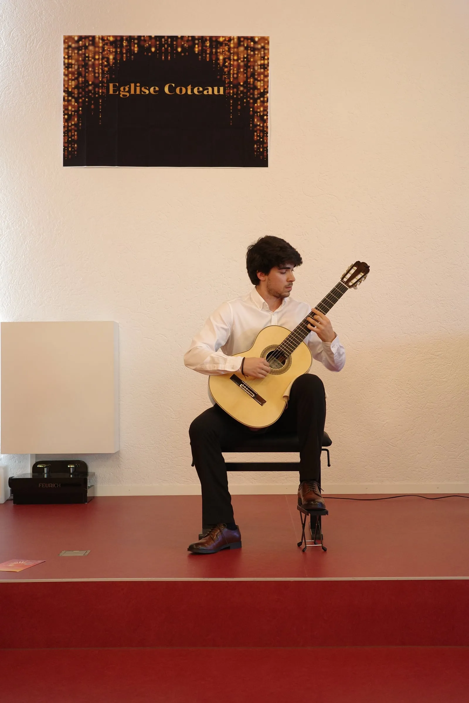 Miguel Ferreira in recital, the concert banner on the wall behind him.